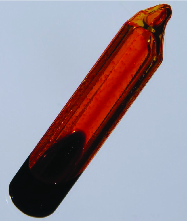 A glass container is shown that is filled with an orange-brown gas and a small amount of dark orange liquid.