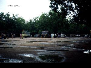 People and vans standing on a gravel-paved area covered with puddles