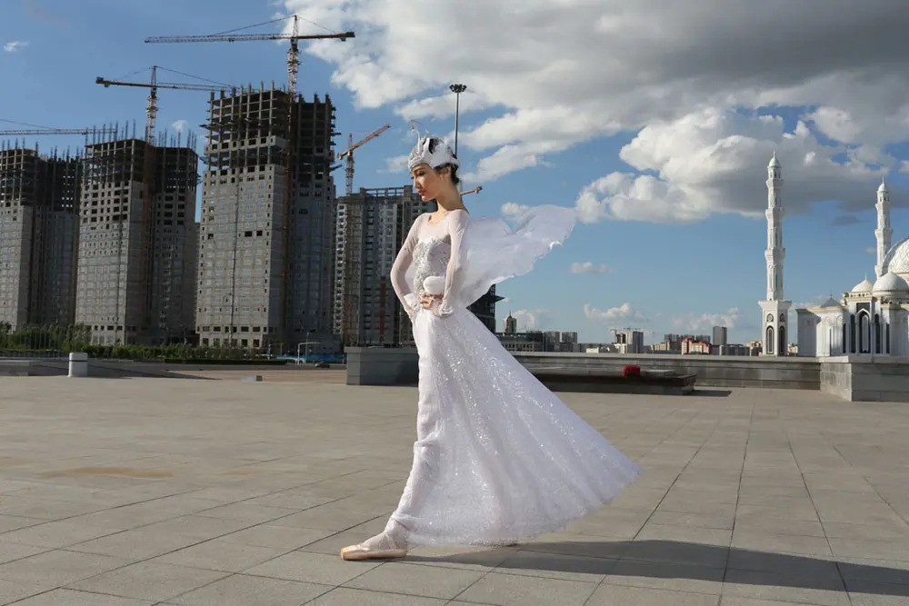 a woman in a white swan costume with new and old buildings in the background