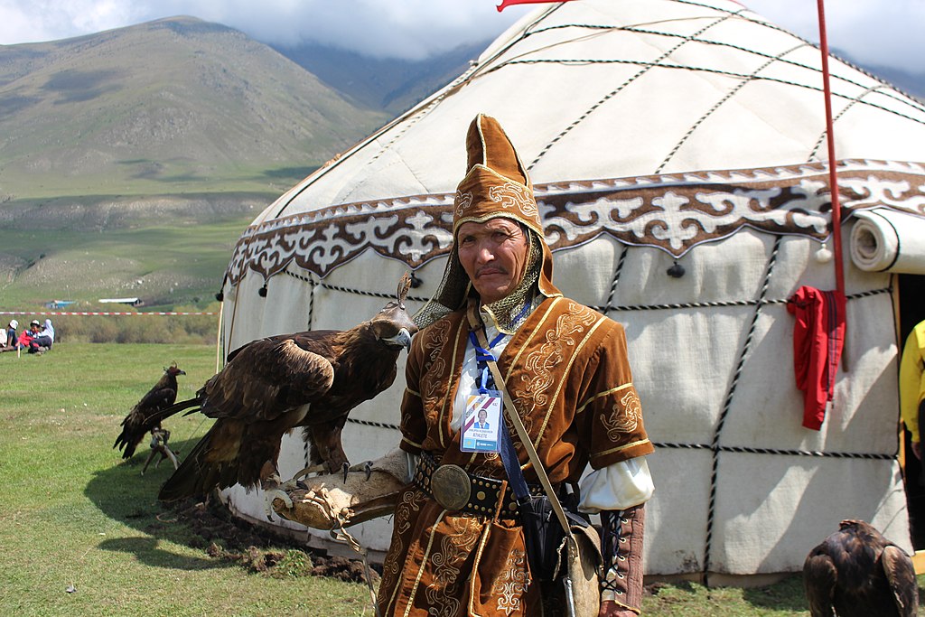 a man in traditional costume holding a golden eagle in front of a yurt