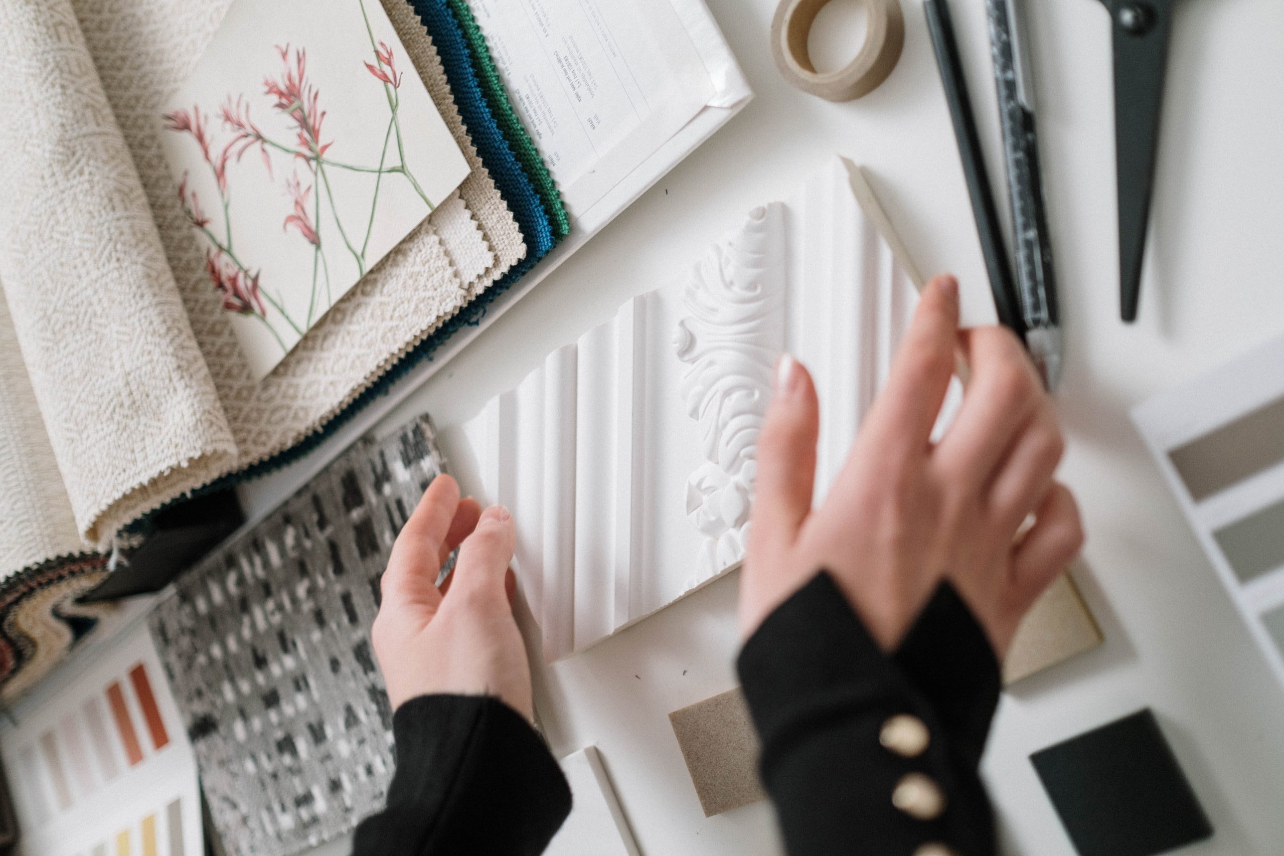 Handing reaching for wall molding sample surrounded by wallpaper swatches and design supplies