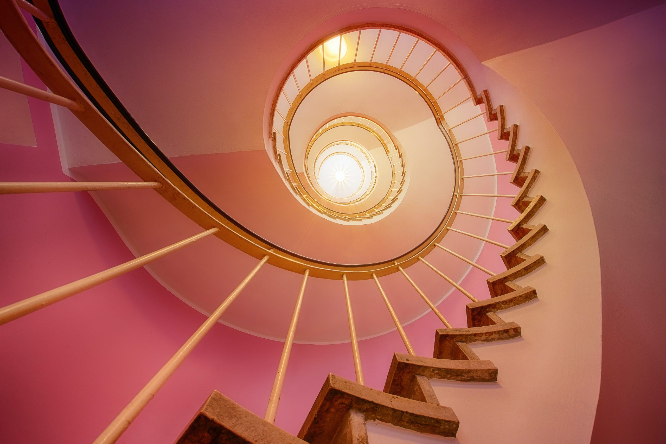 The view from the bottom of a spiral staircase going up bubblegum pink walls