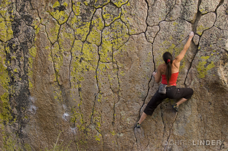 Athletic female climber climbs boulder at Buttermilk Boulders, near Bishop, California.